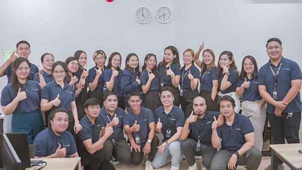 Outdesk team members in a large group smiling at the camera with thumbs up